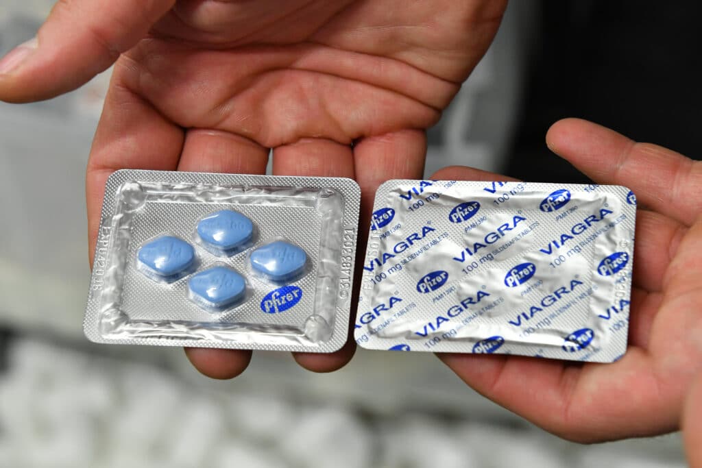 Két kézben tartott viagra 100 mg bliszter: bal oldalt négy kék, rombusz alakú tabletta, jobb oldalt VIAGRA feliratú fólia.