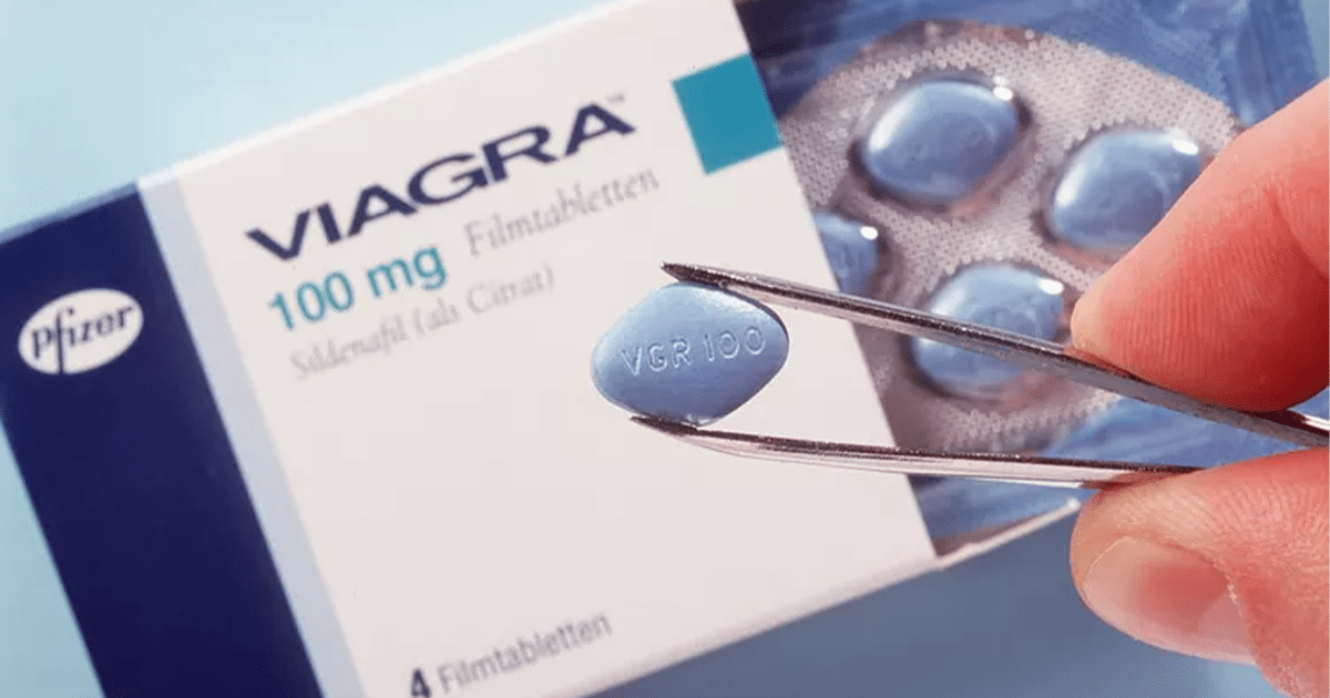 Csipesszel tartott viagra 100 mg tabletta közelről, a doboz és bliszter előtt.